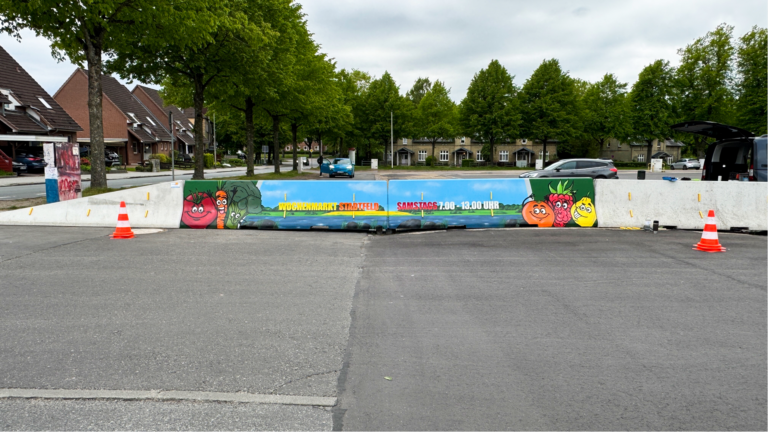 Kunst am Schleswiger Interims-ZOB: Graffiti gestaltet Absperrelemente und wirbt für den Wochenmarkt